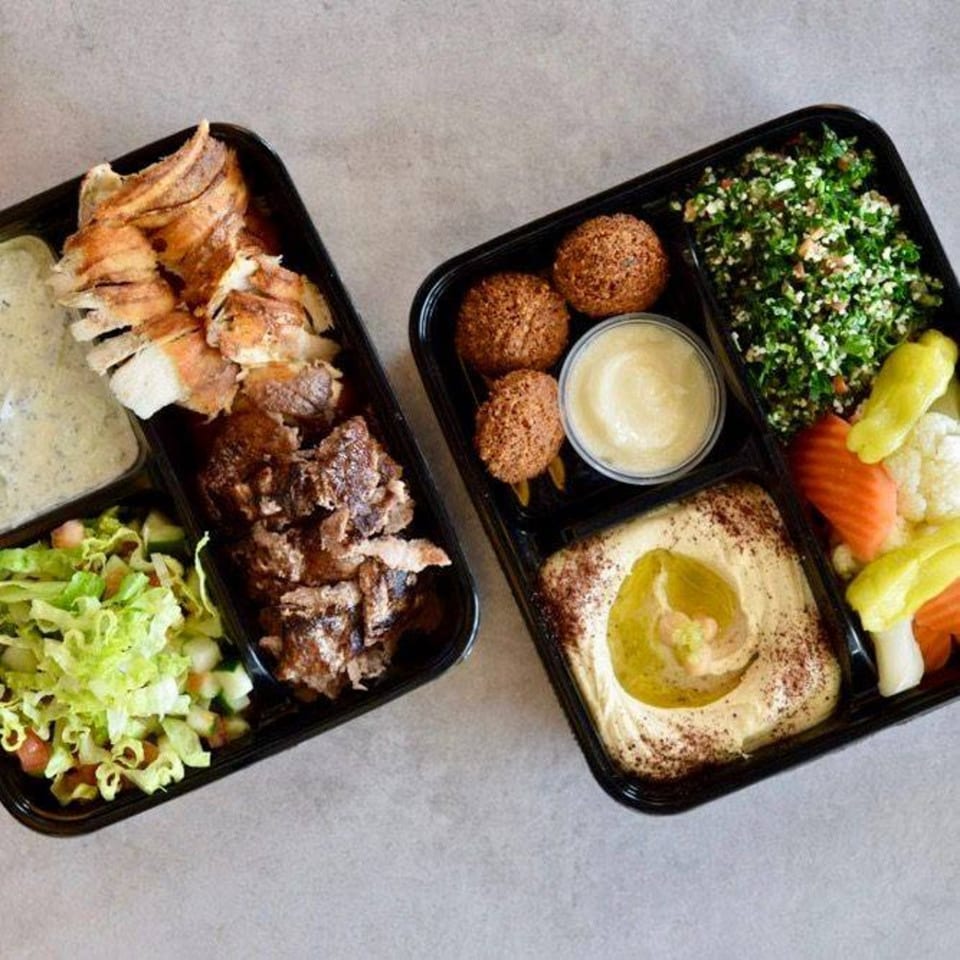 Two Mediterranean Shawarma Press takeout containers filled with chicken, beef, falafel, hummus, tabbouleh, and salad.