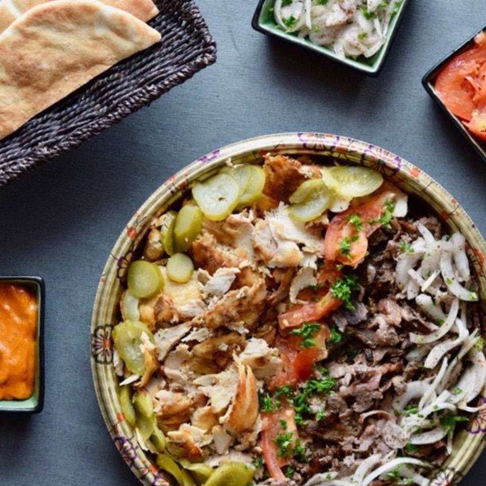 Shawarma Press's chicken and beef shawarma platter with pickles, tomatoes, onions, and pita bread.