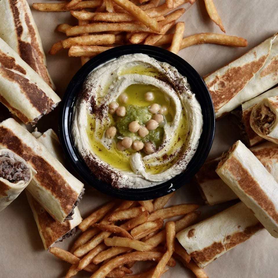 Shawarma Press Mediterranean meal with hummus, shawarma wraps, and French fries on a brown surface.