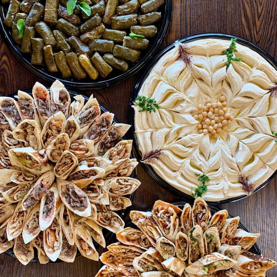Platters of Shawarma Press's Mediterranean food, including grape leaves, hummus, and shawarma wraps.
